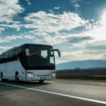 White Modern comfortable tourist bus driving through highway at bright sunny sunset.