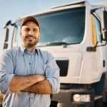 Happy confident male driver standing in front on his truck and looking at camera.