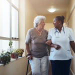 Portrait of smiling healthcare worker walking and talking with senior woman